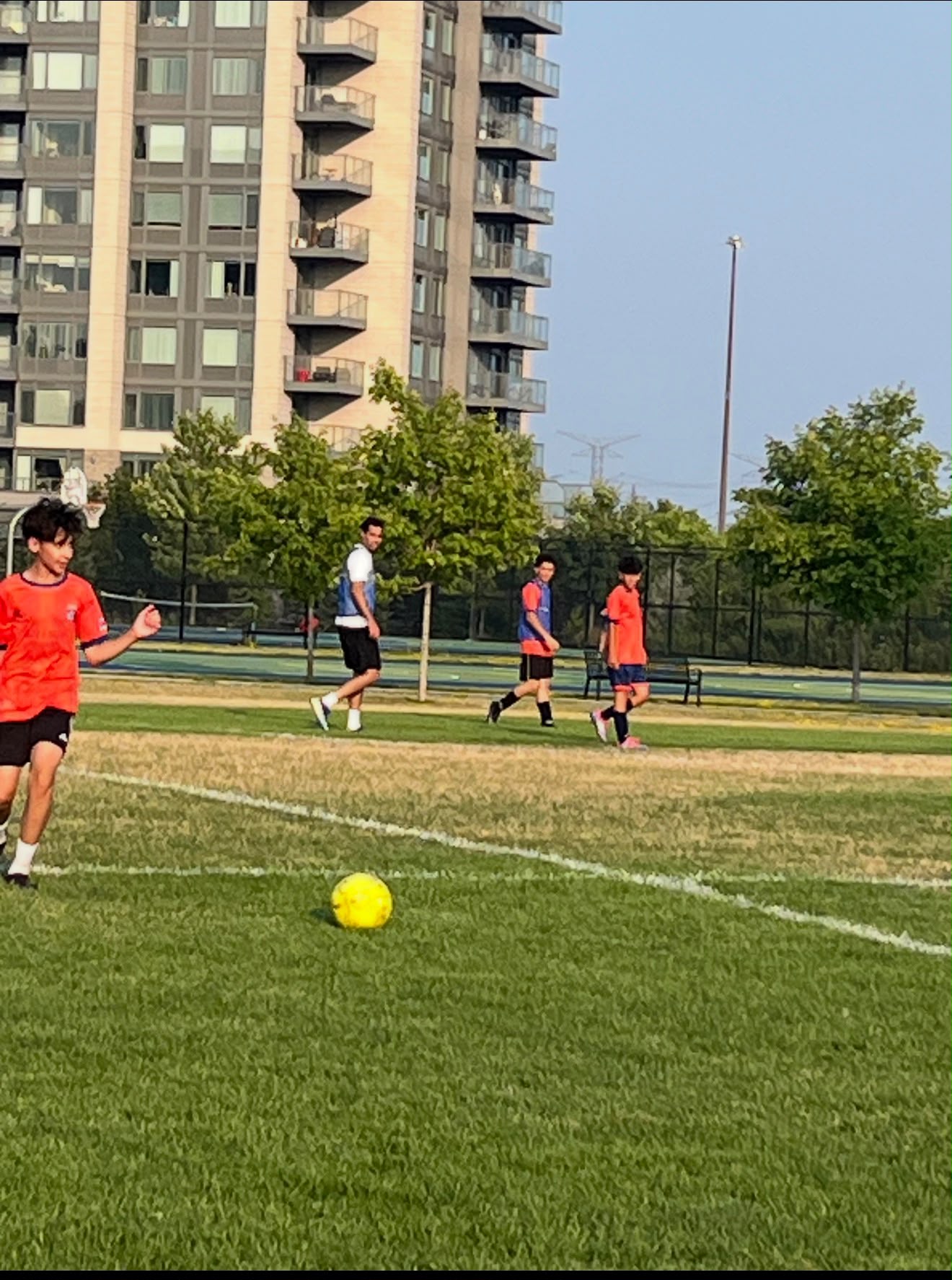 Children sprint across a worn community football pitch in Toronto during an after-school session